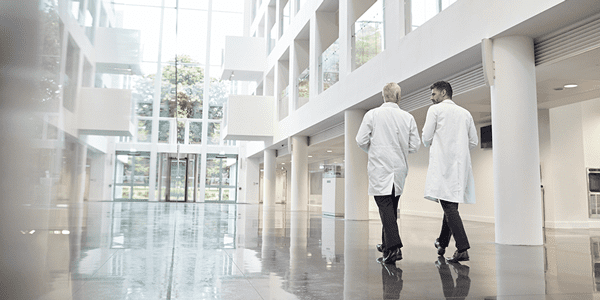 Two doctors walking down a open hall  with their backs to you
