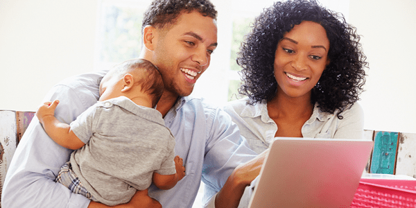 A man and woman holding a baby while looking at a computer
