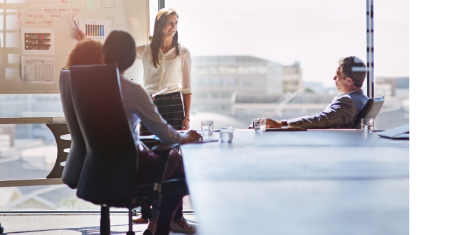 Group of people sitting at a conference watching a woman give a presentation