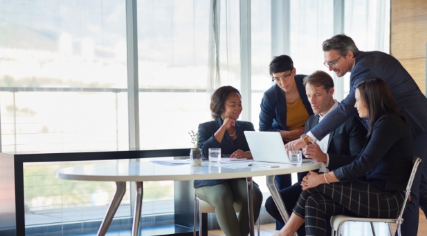 Another group of people standing around a table looking at a laptop