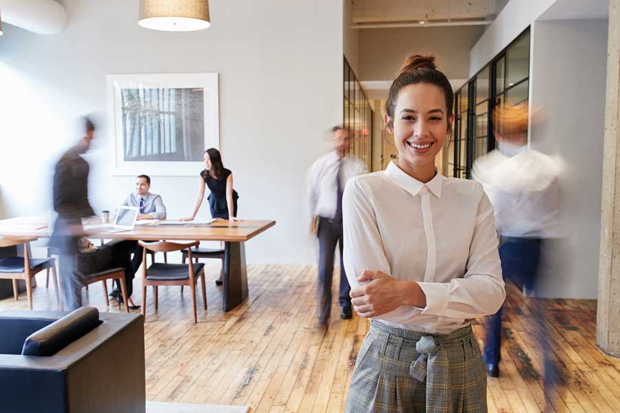 A woman standing in a office with people busy around her